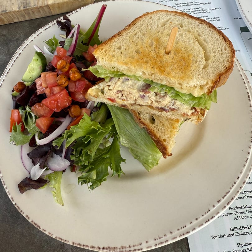 A Sage Social Eatery chicken salad sandwich on toasted bread with a side salad.